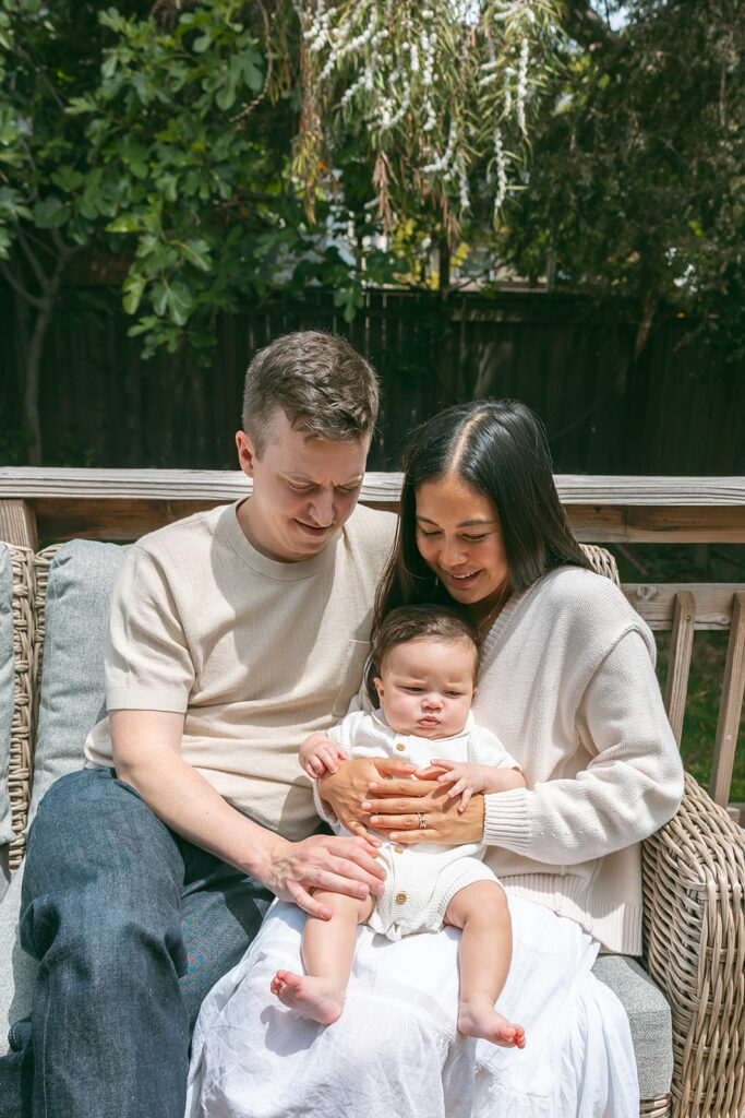 Family of three sitting on their outdoor patio with their small baby for their at-home family photos in Oakland, California. 