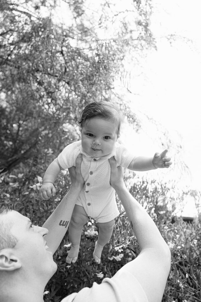 Black and white photo of a father holding up his small baby in the air. 