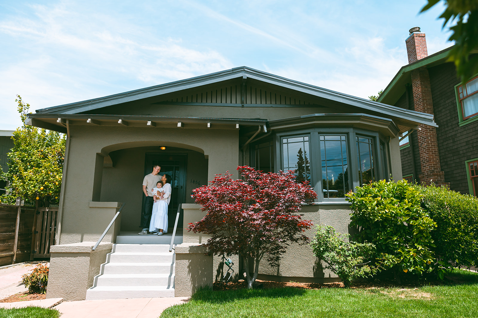 Wide shot of a family of three posing on their front porch as the photographer leaves their at-home family photos in Oakland, California. 