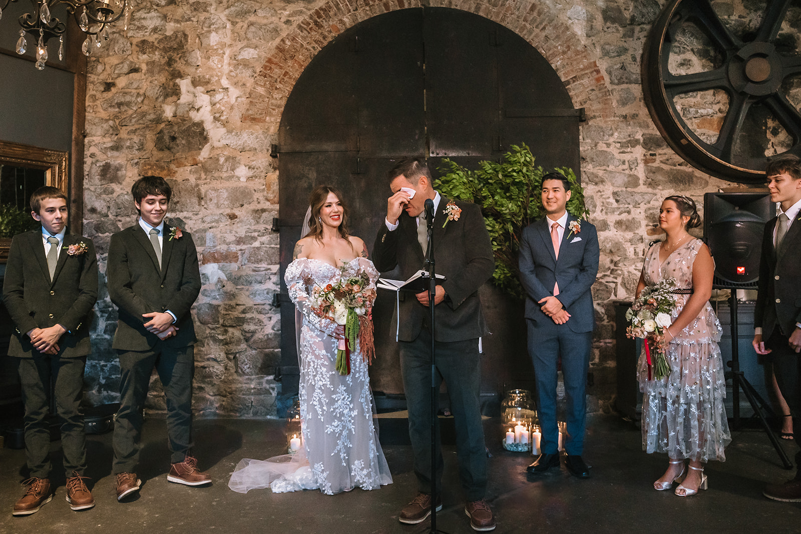 Groom wiping away tears during vows while bride smiles at Miners Foundry wedding in Nevada City, California.