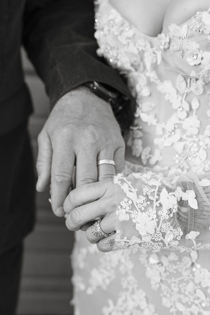 Black and white close up portrait of a bride and groom holding hands while showing their wedding rings. 