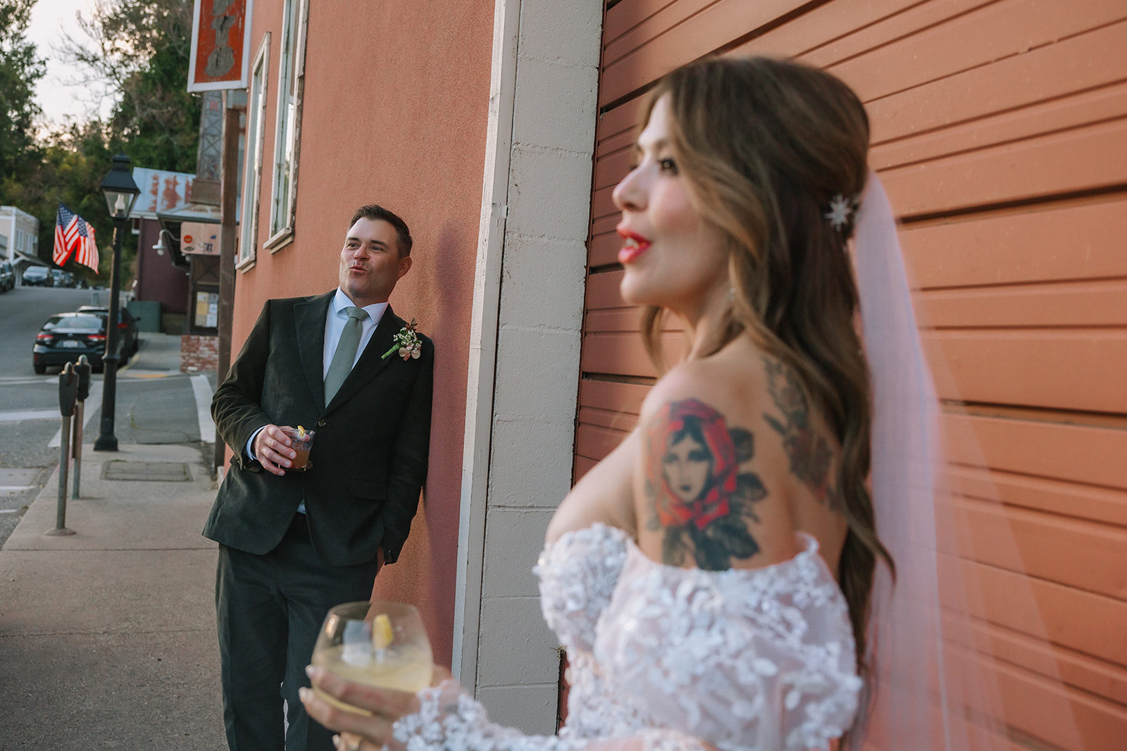 Bride and groom holding drinks and laughing along downtown Nevada City street during golden hour portraits at Miners Foundry wedding in California.