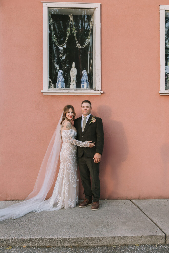 Bride and groom posing in front of blush colored wall during golden hour portraits at Miners Foundry wedding in Nevada City, California.