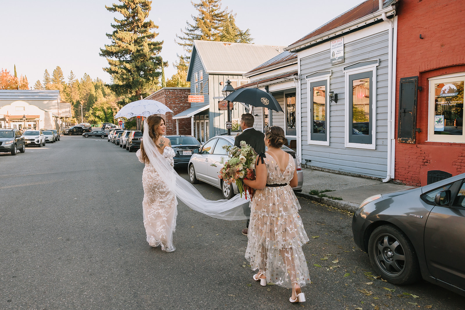 Bride walking down Nevada City street holding umbrella during marching band processional at Miners Foundry wedding in Nevada City, California.