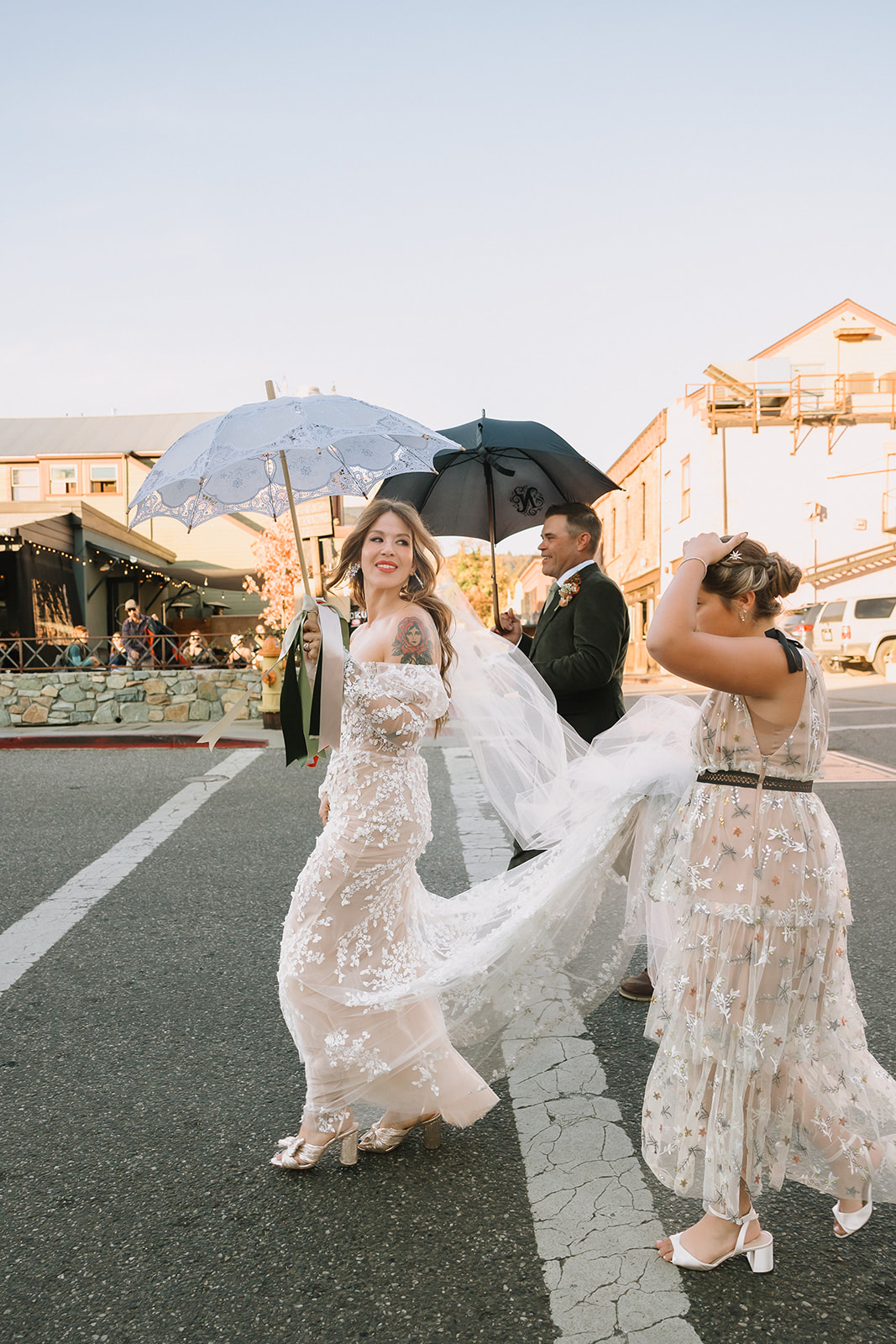 Bride walking across street with veil flowing during marching band processional at Miners Foundry wedding in Nevada City, California.
