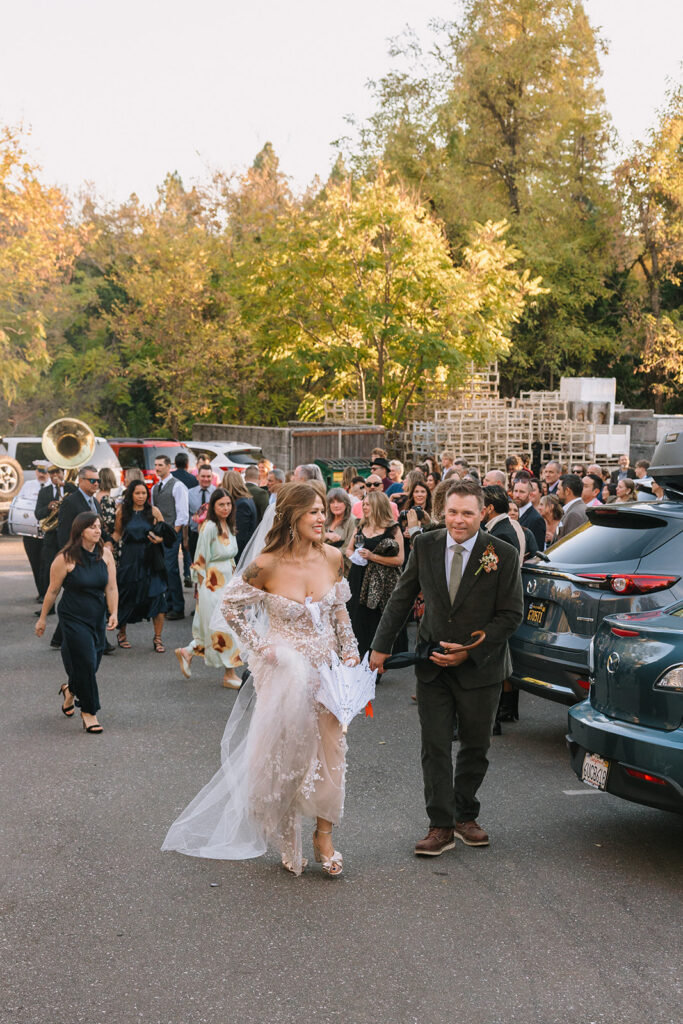 Bride and groom walking with guests behind them during wedding processional through downtown Nevada City at Miners Foundry wedding in California.