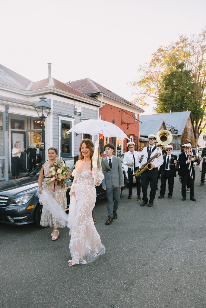 Bride leading marching band processional through downtown Nevada City with guests following during Miners Foundry wedding in California.