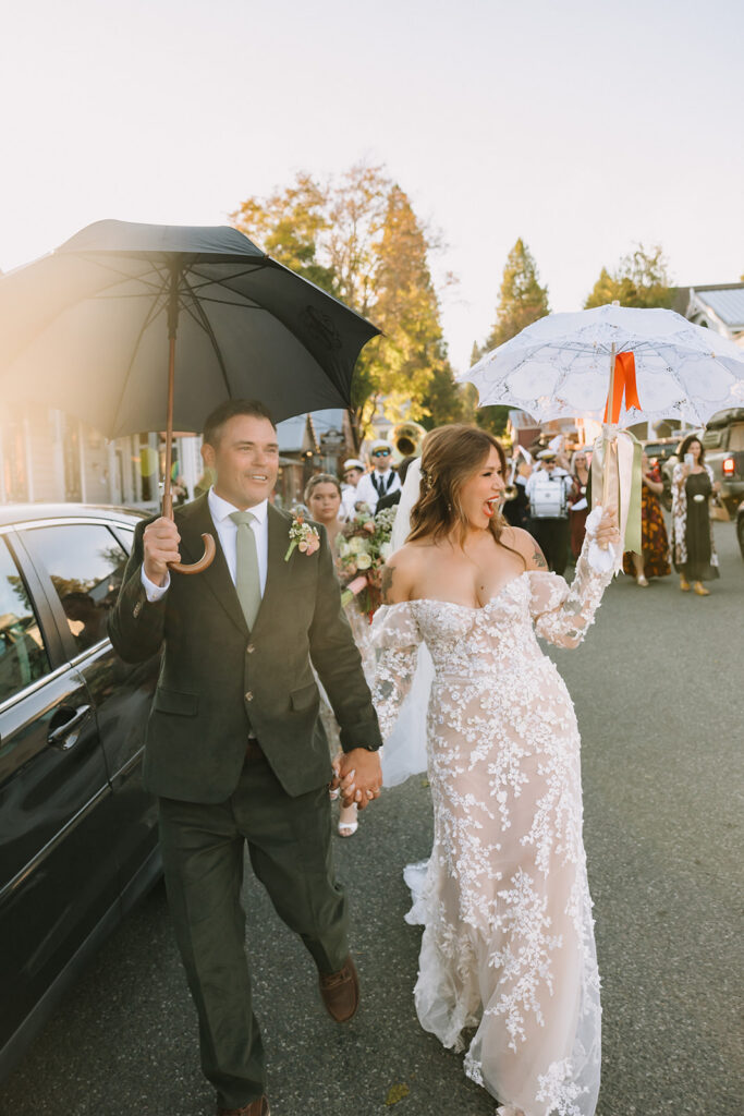 Bride and groom laughing and celebrating while walking with groom during marching band processional at Miners Foundry wedding in Nevada City, California.