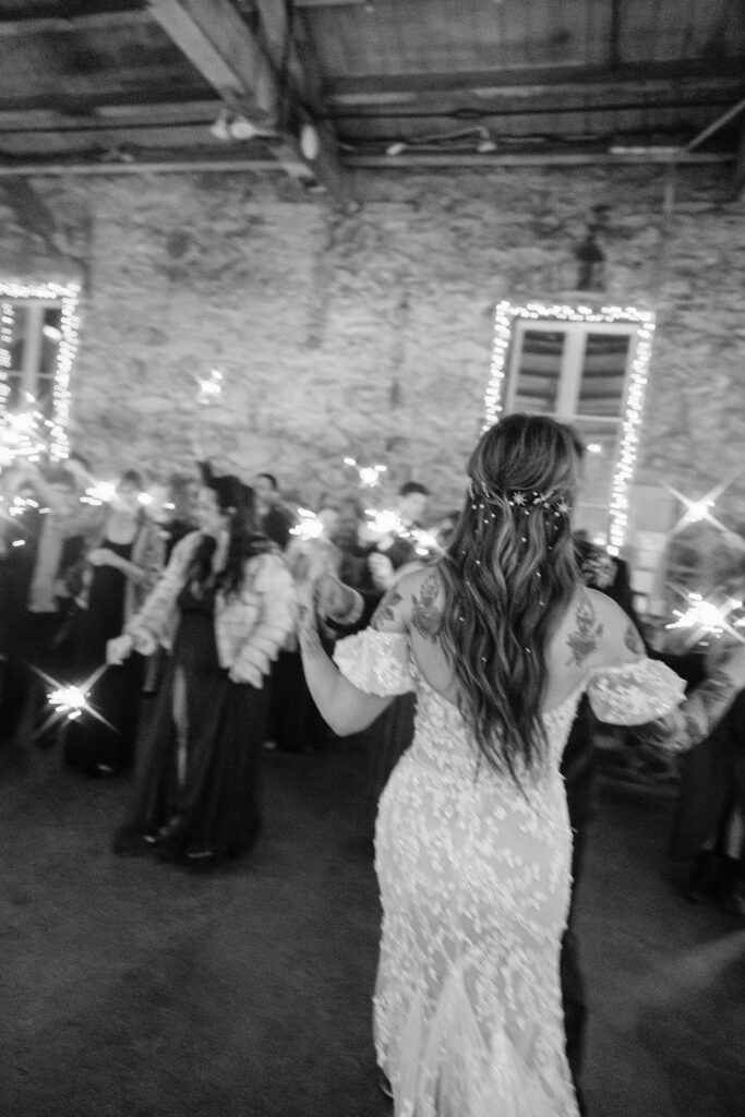 Black and white photo of a bride and groom dancing while guests hold sparklers in the air. 