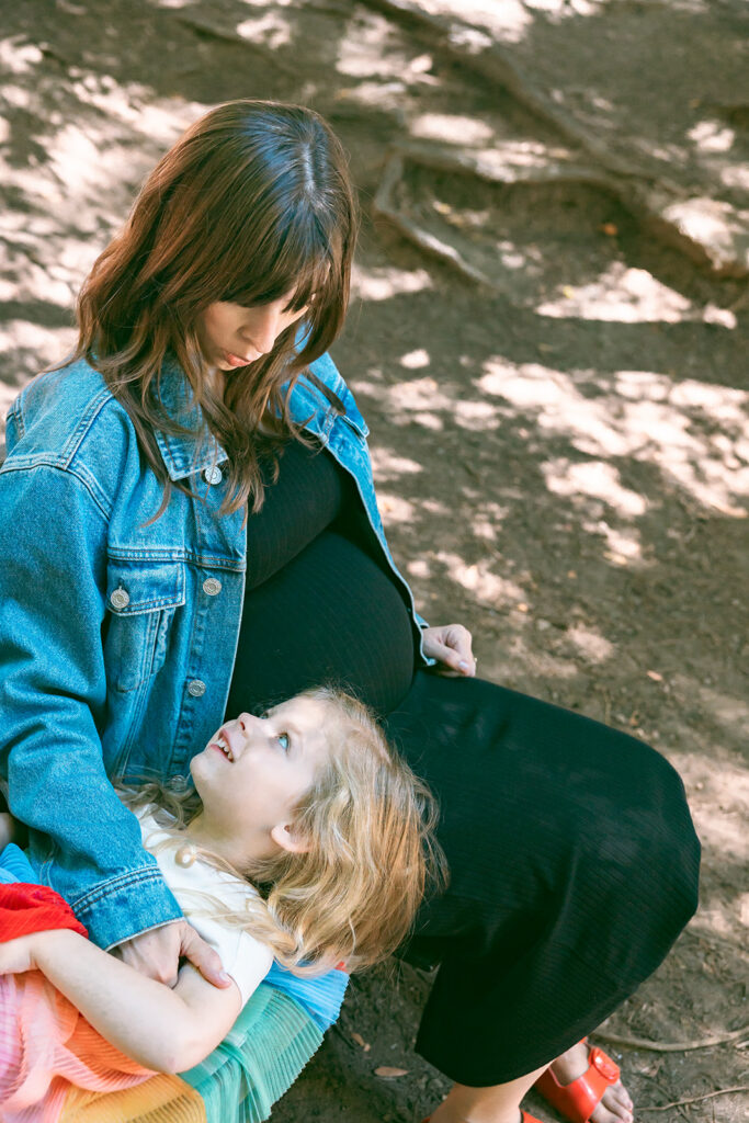 Little girl laying on her pregnant mothers lap at Old Mill Park in Marin County. 
