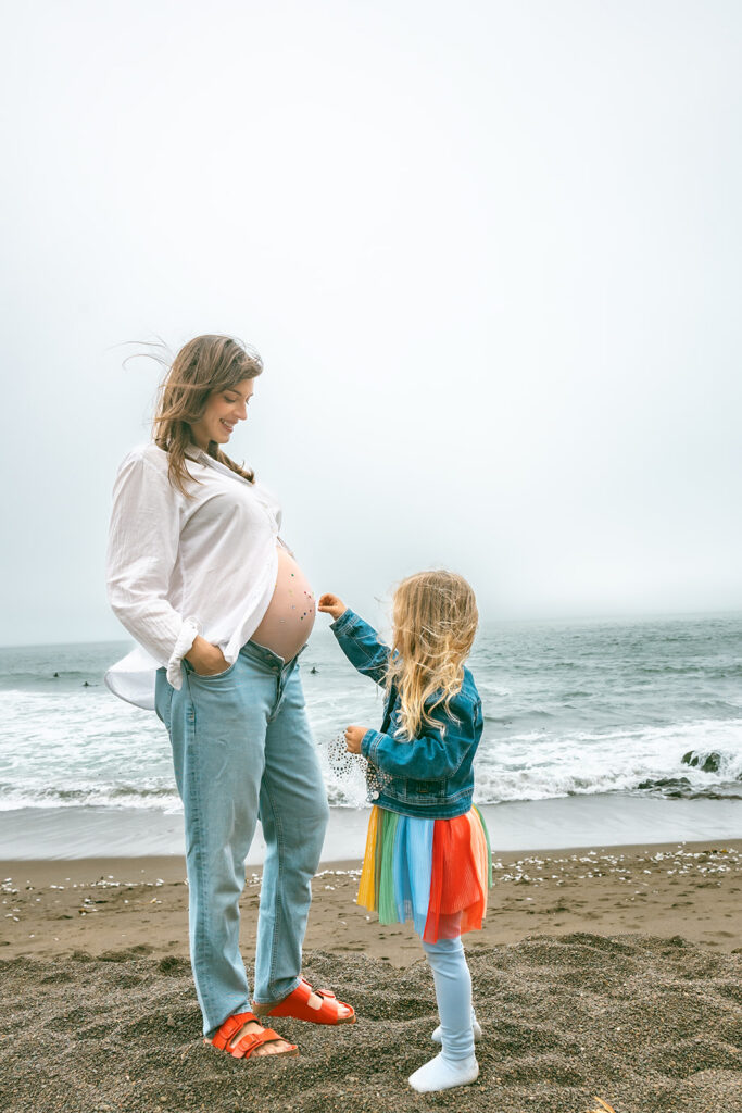  Little girl decorating her pregnant mothers belly with jewels on Rodeo Beach. 