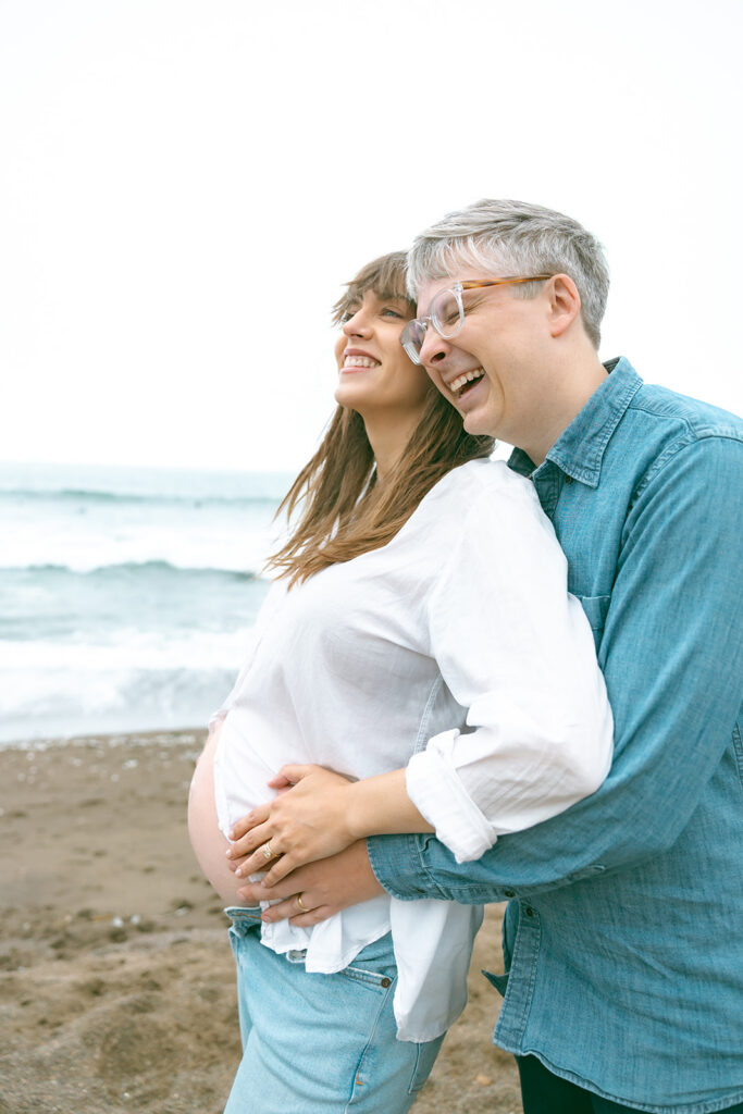 Close maternity portrait of couple laughing together by the ocean at Rodeo Beach.