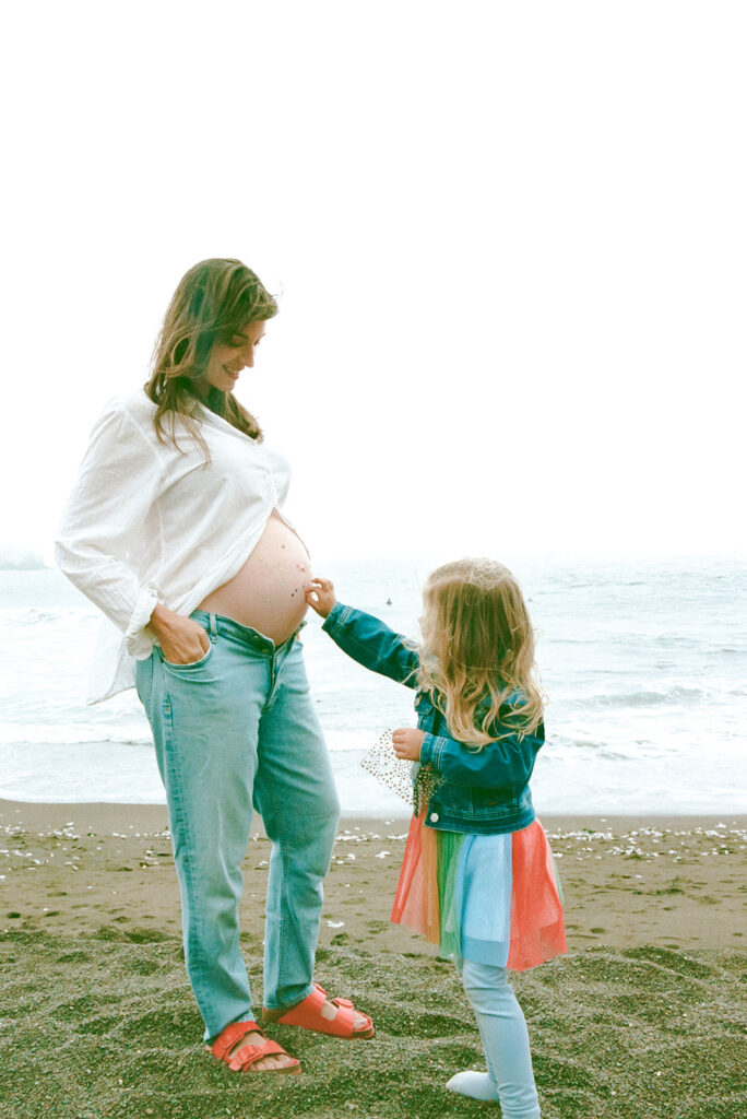 Mother and daughter adding jewels to pregnant belly during Rodeo Beach maternity session.