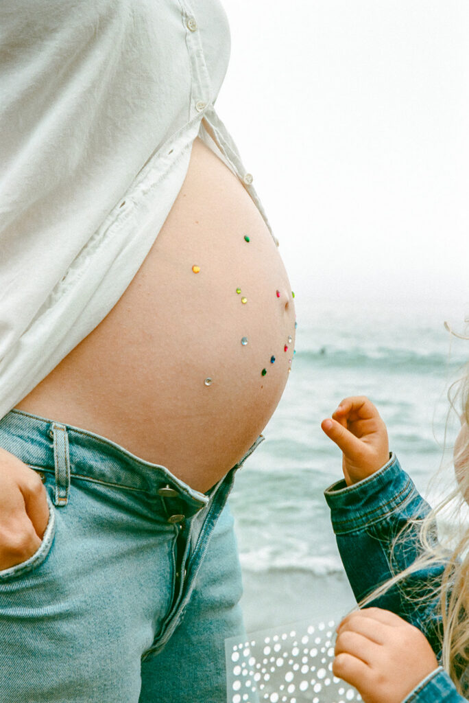 Little girl decorating her mothers pregnant belly with jewels at Rodeo Beach in the Marin Headlands. 