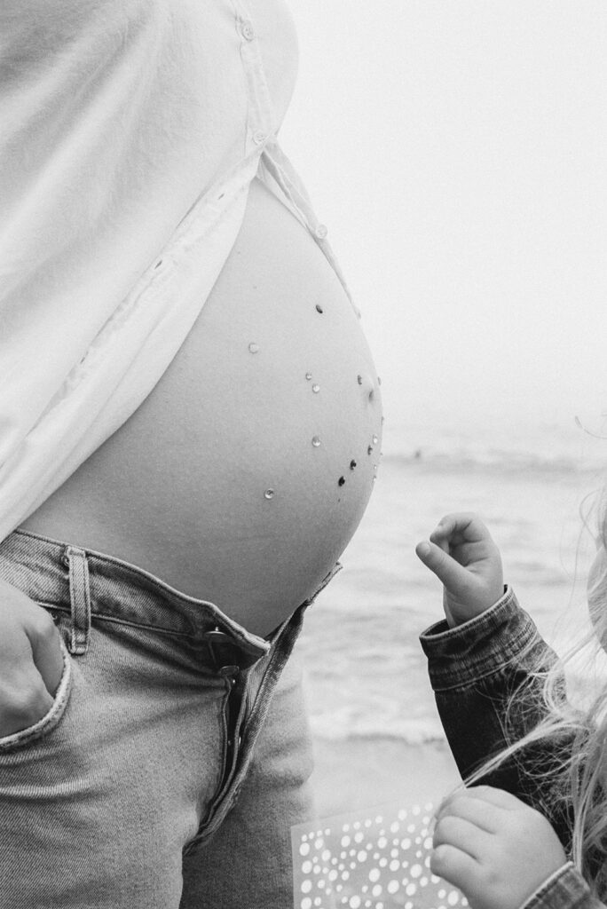Black and white 35mm film photo of a little girl decorating her mothers pregnant belly with jewels. 