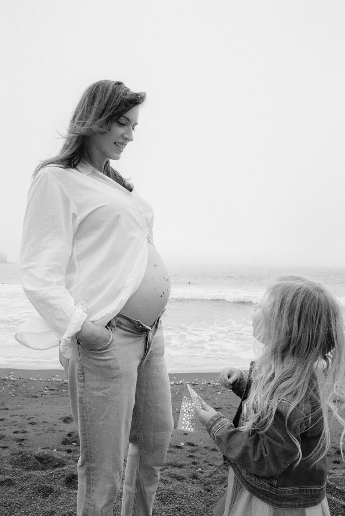 Black and white 35mm film photo of a little girl and her pregnant mother on Rodeo Beach, 