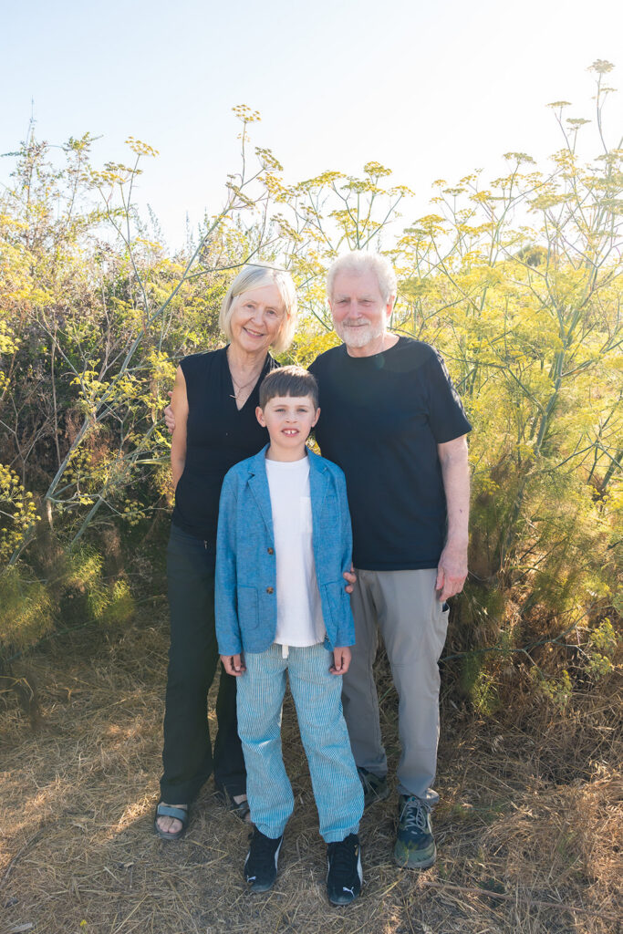 Grandparents posing with their grandson in front of wild flowers. 