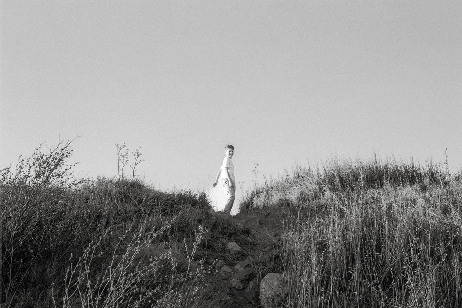 Black and white wide shot of a young boy walking the trails at Albany Bulb. 