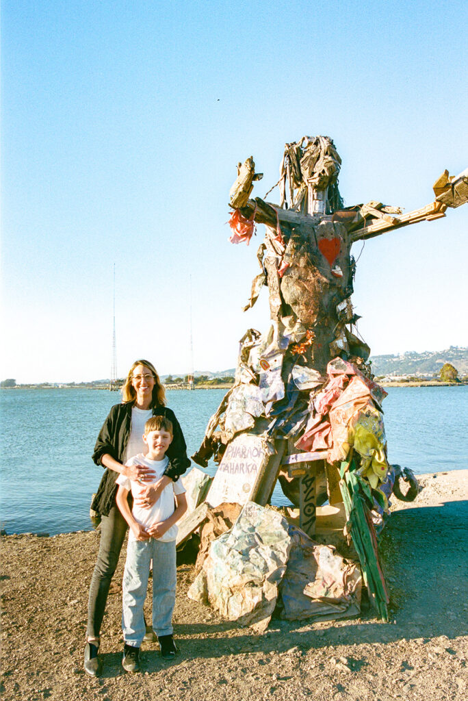 Mother and son standing beside colorful driftwood sculpture at Albany Bulb on film.