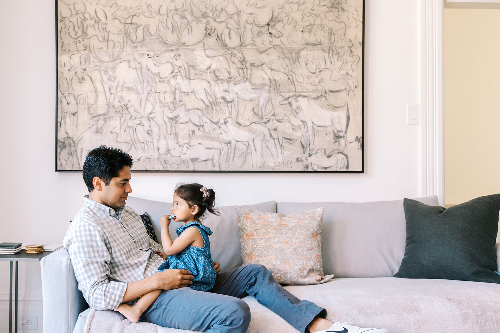 Father holding his toddler daughter in his lap on the couch during their at-home family photos.
