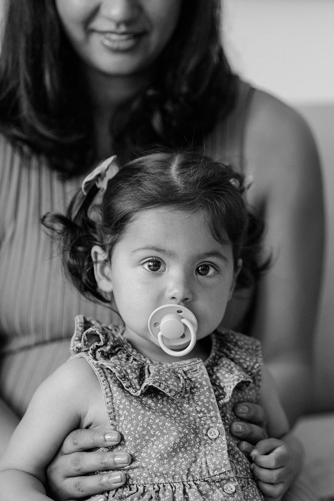 Close up black and white portrait of a little girl being held by her mother during their at-home family photos in San Francisco. 