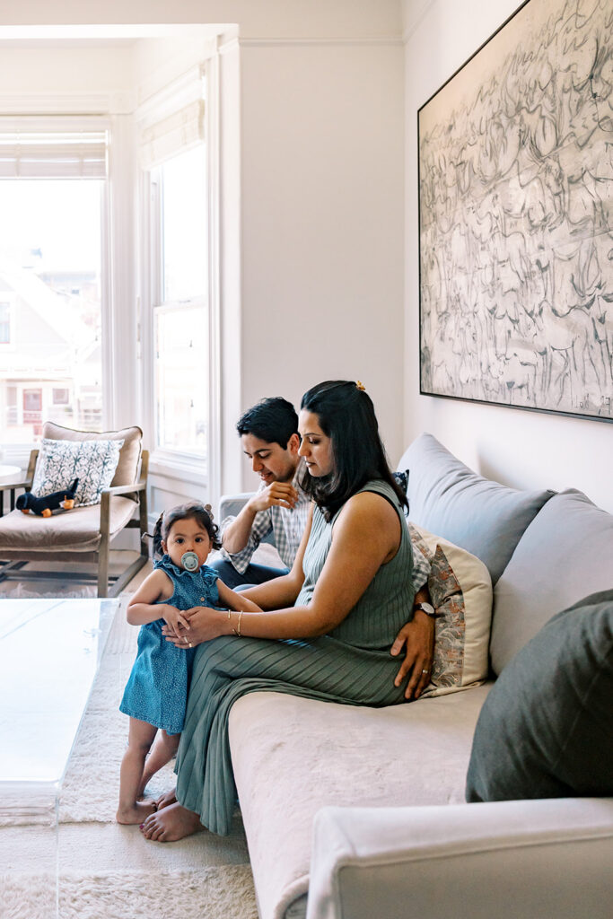 Family of three posing on the couch during their at-home family San Francisco maternity photos.