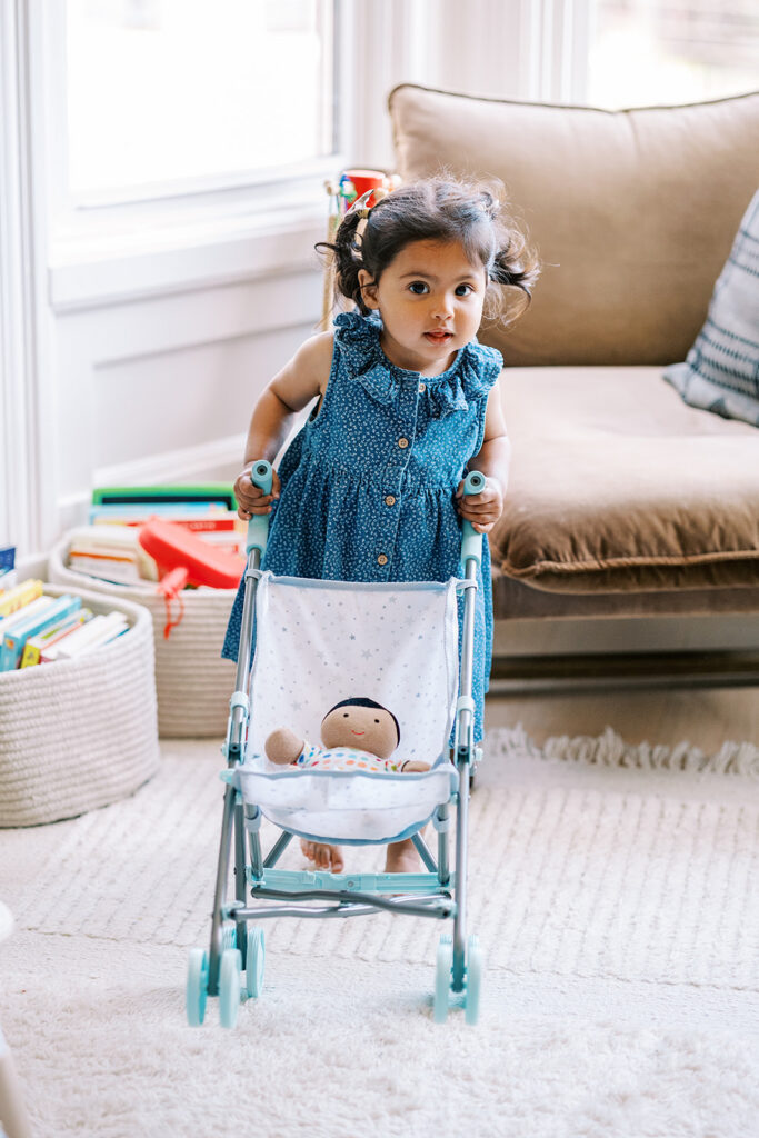 Little girl walking around the house and pushing her baby doll in a stroller during at-home San Francisco family photos.