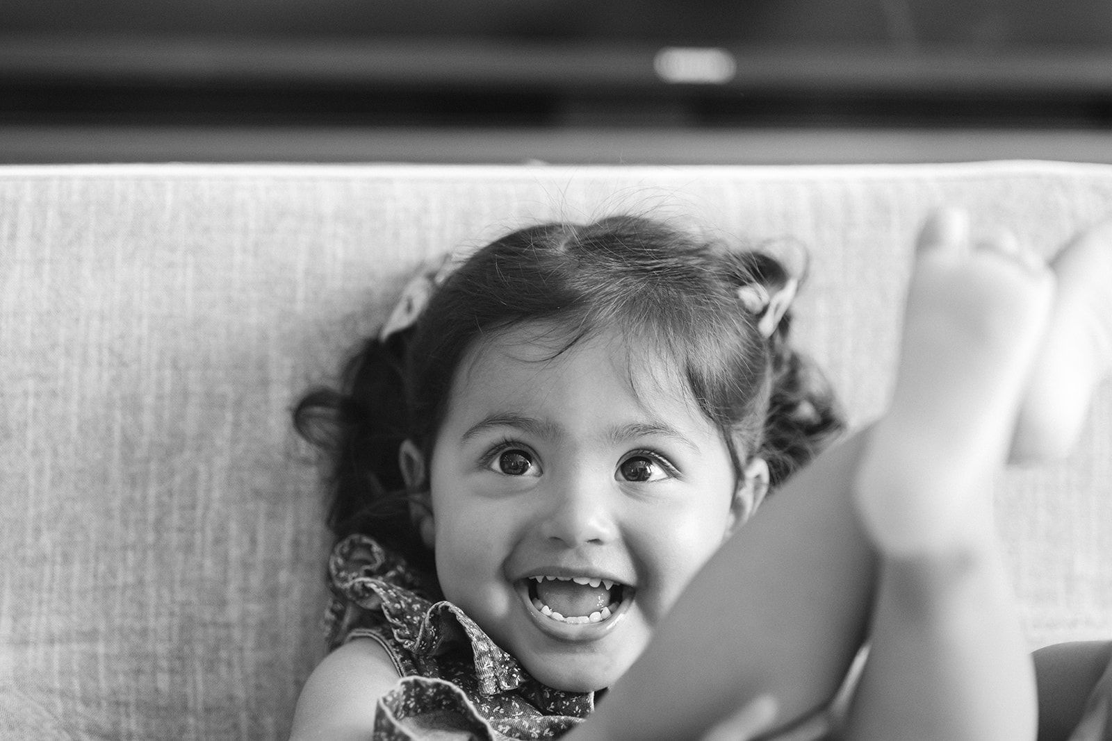 Black and white close up photo of a little girl sitting in front of her couch.