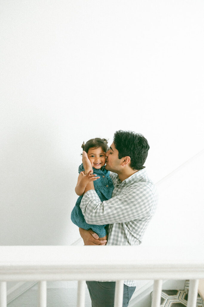 Father kissing his toddler daughter on the stairs of their home.