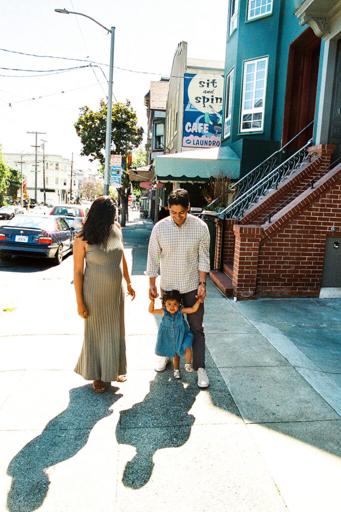 Family of three walking through their neighborhood during family and San Francisco maternity photos. 