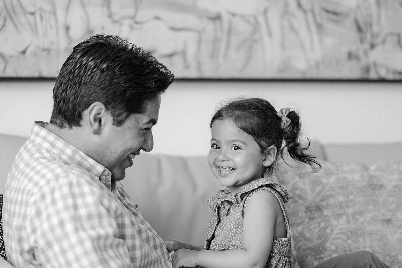 Black and white photo of a father and daughter smiling on the couch during at-home family photos in San Francisco.