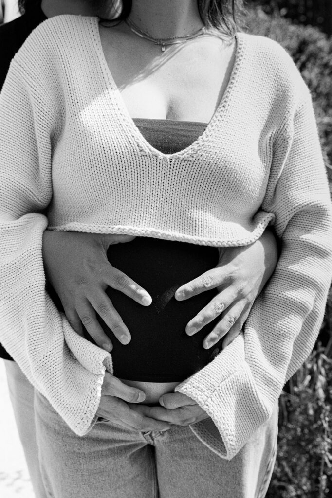 Close up black and white photo of a man holding his pregnant partners belly.