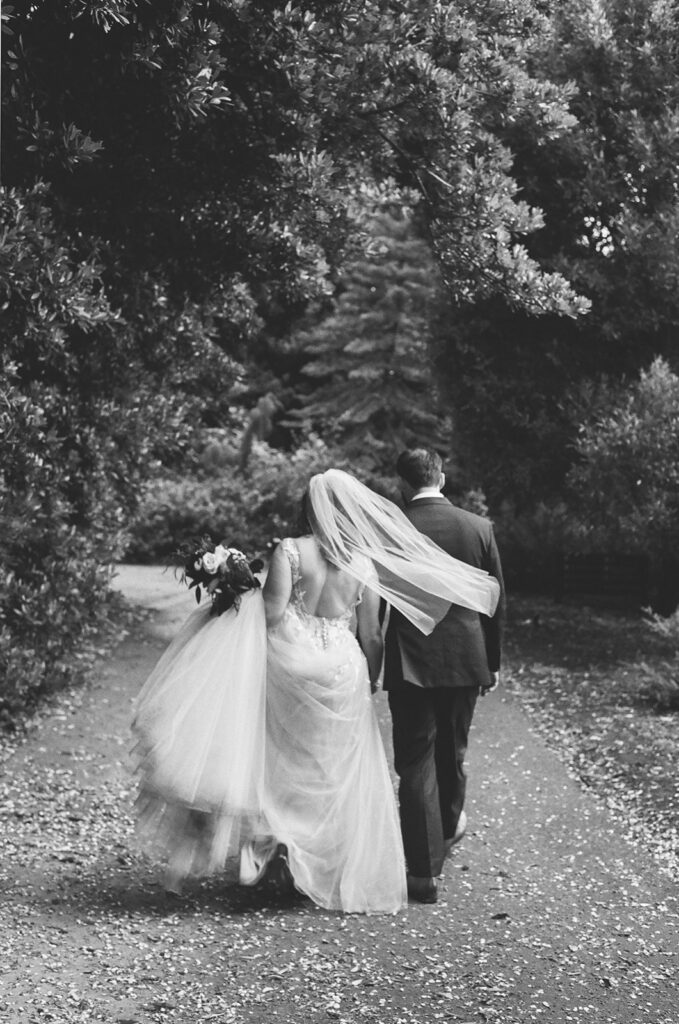 Black and white film photo of a bride and groom walking through San Francisco Botanical Garden.