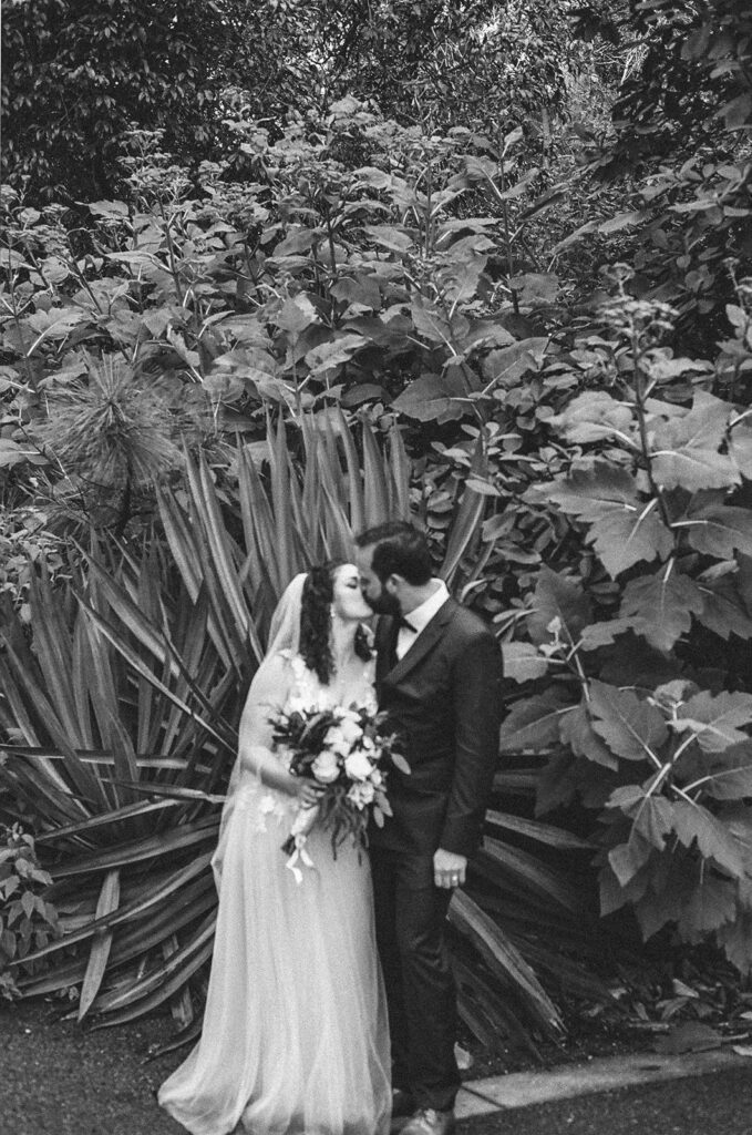 Black and white film photo of a bride and groom kissing at San Francisco Botanical Garden.