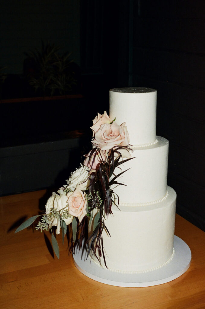 Film photo of a three-tiered white wedding cake with floral accents.