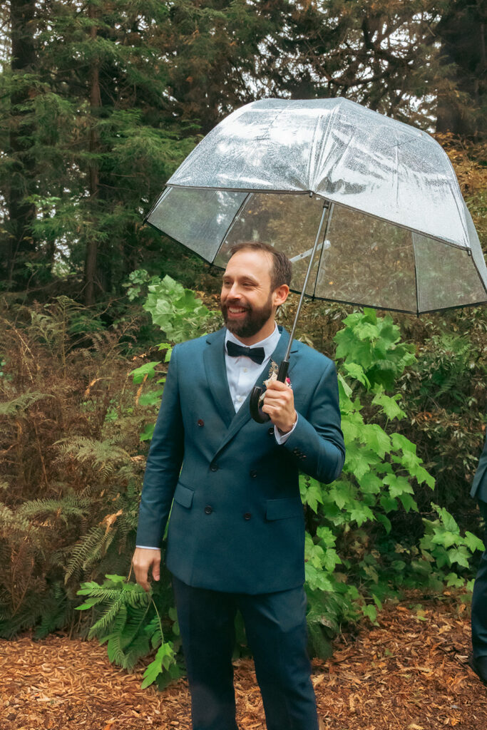 Groom holding a see through umbrella before his San Francisco Botanical Garden wedding ceremony in Redwood Grove.