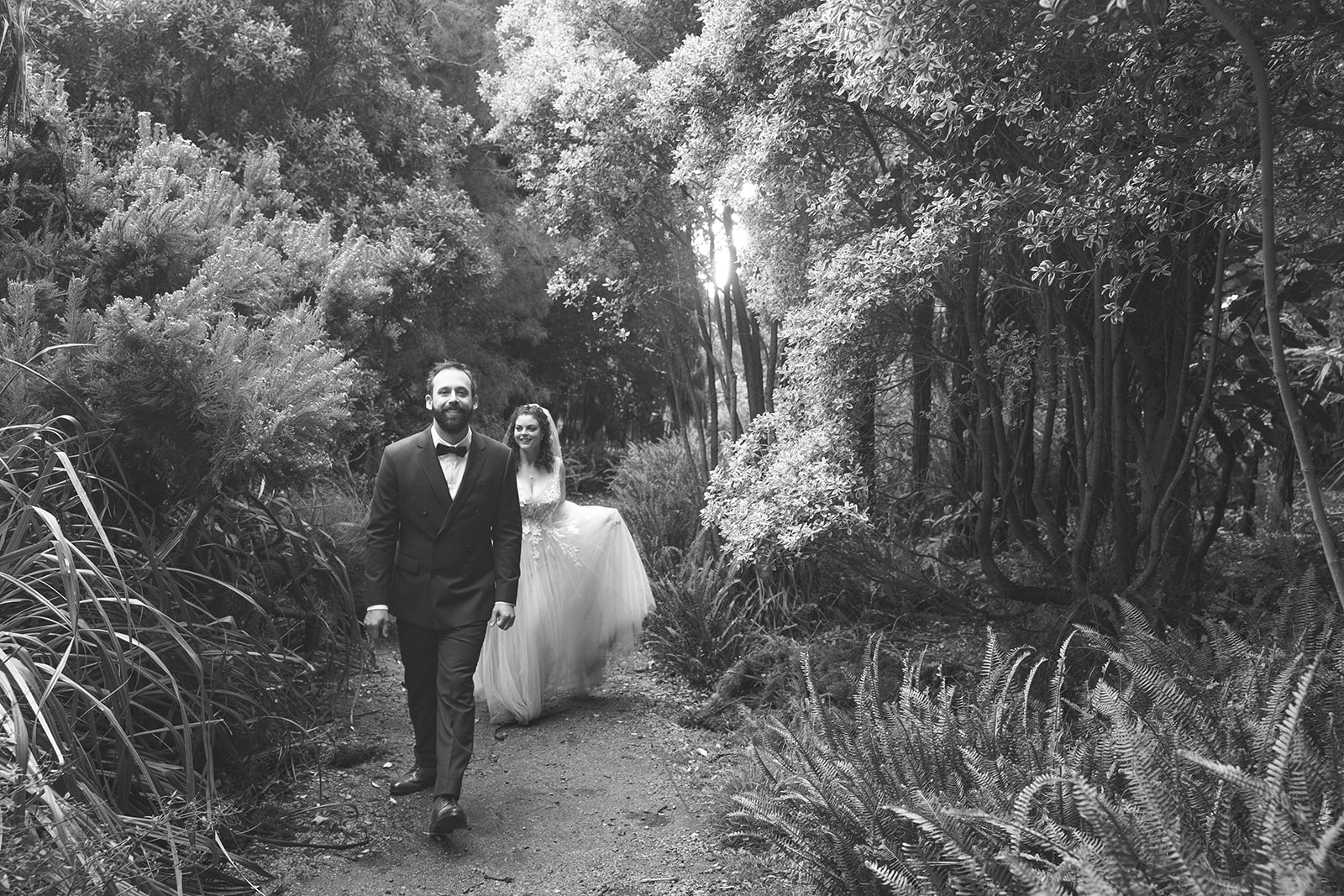 Black and white photo of a bride and groom walking through the San Francisco Botanical Garden.
