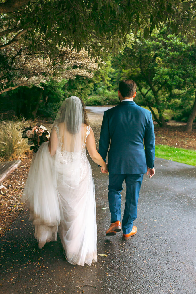 Bride and groom holding hands and walking down a path after their San Francisco Botanical Garden wedding.
