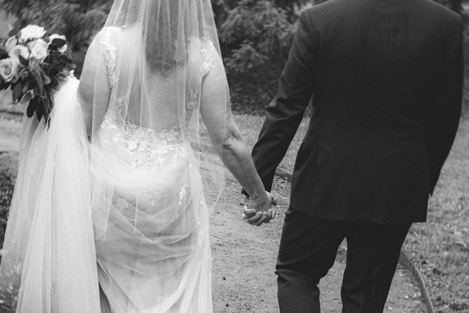 Close up black and white photo of a bride and groom holding hands and walking together.
