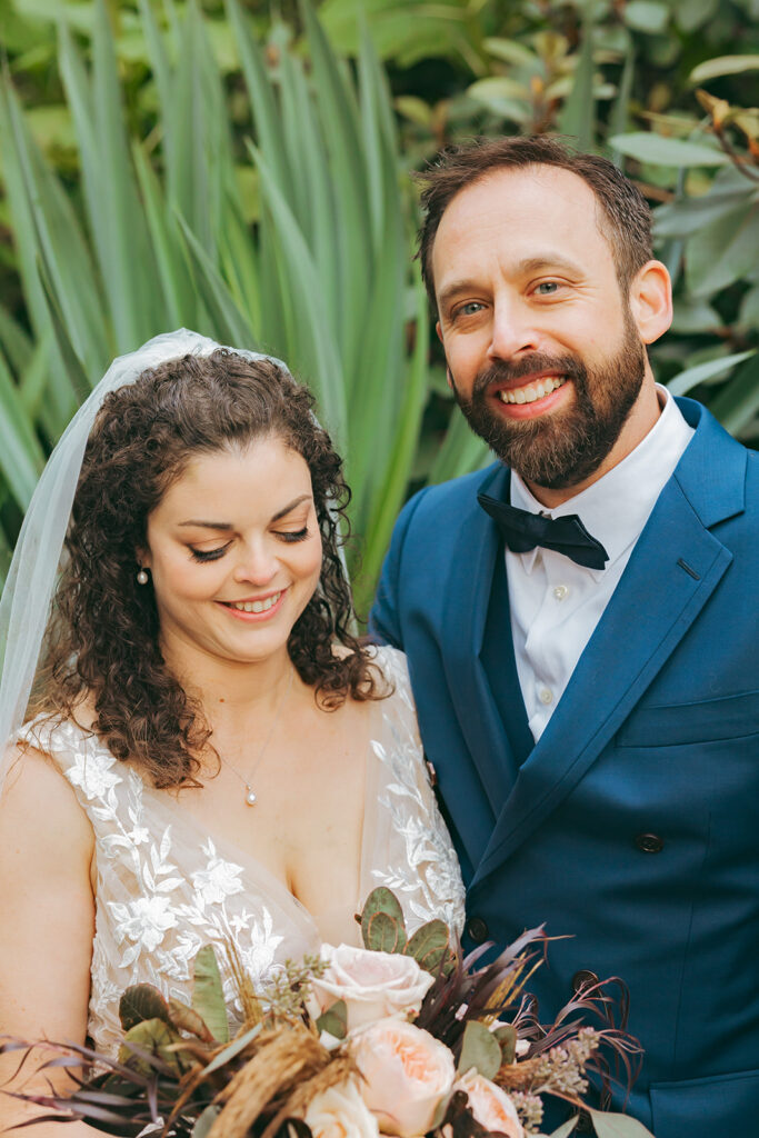 Bride and groom smiling in front of greenery.