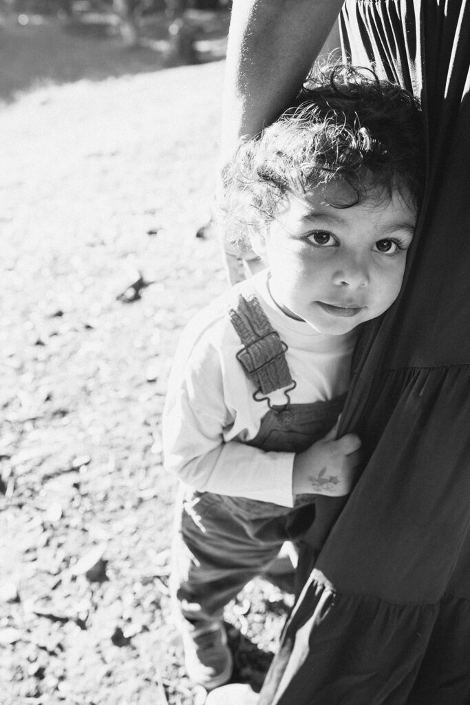 Black and white photo of a young boy holding onto his mother and smiling at the camera.