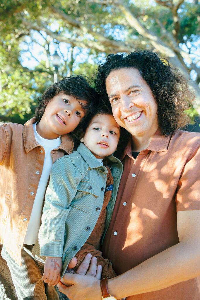 Father smiling with his two sons beneath the trees during a family photo session in the East Bay.