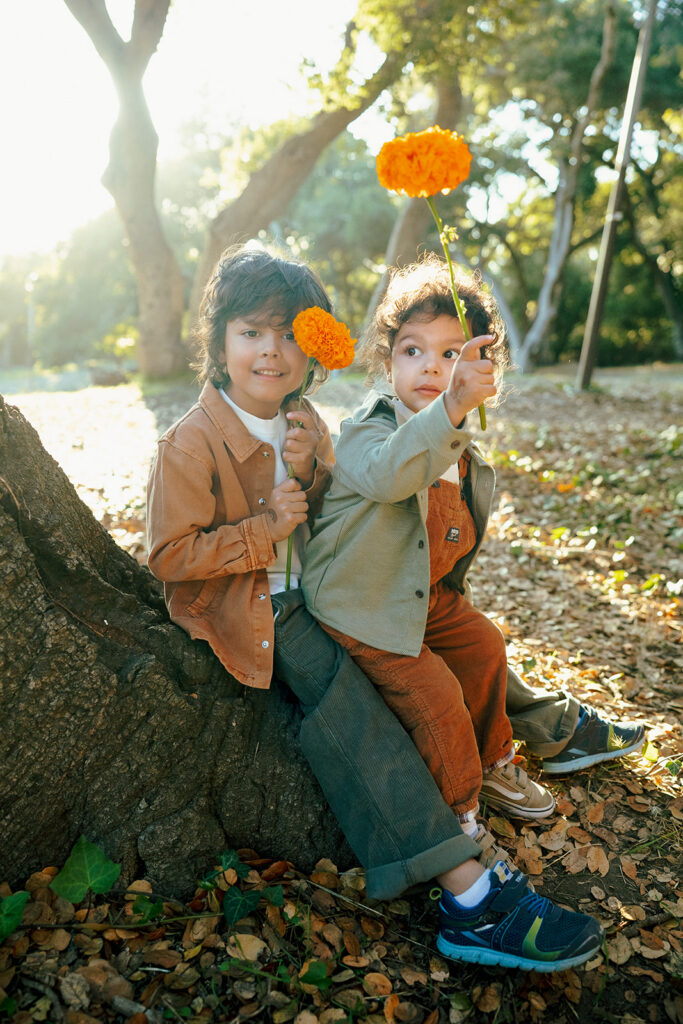 Two young brothers holding orange flowers under oak trees at John Hinkel Park.