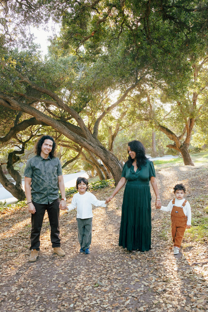 Family of four holding hands beneath oak trees during East Bay family photos at John Hinkel Park.