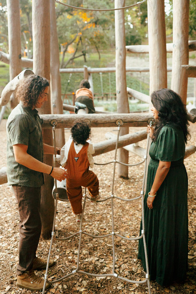Parents watching their children climb and play at John Hinkel Park during a family photo session.