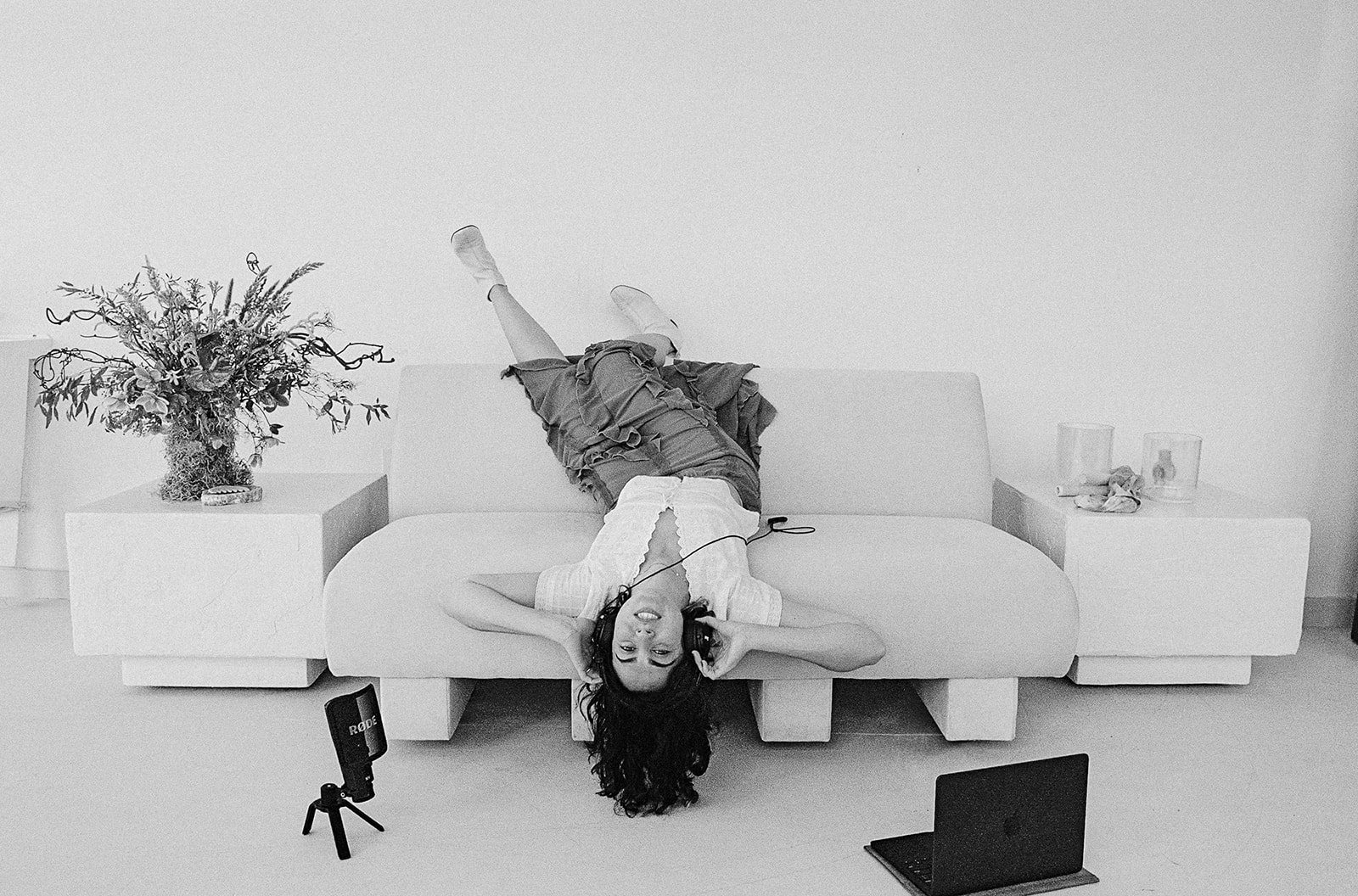 Black and white film photo of a therapist laying upside down on a couch with headphones on.