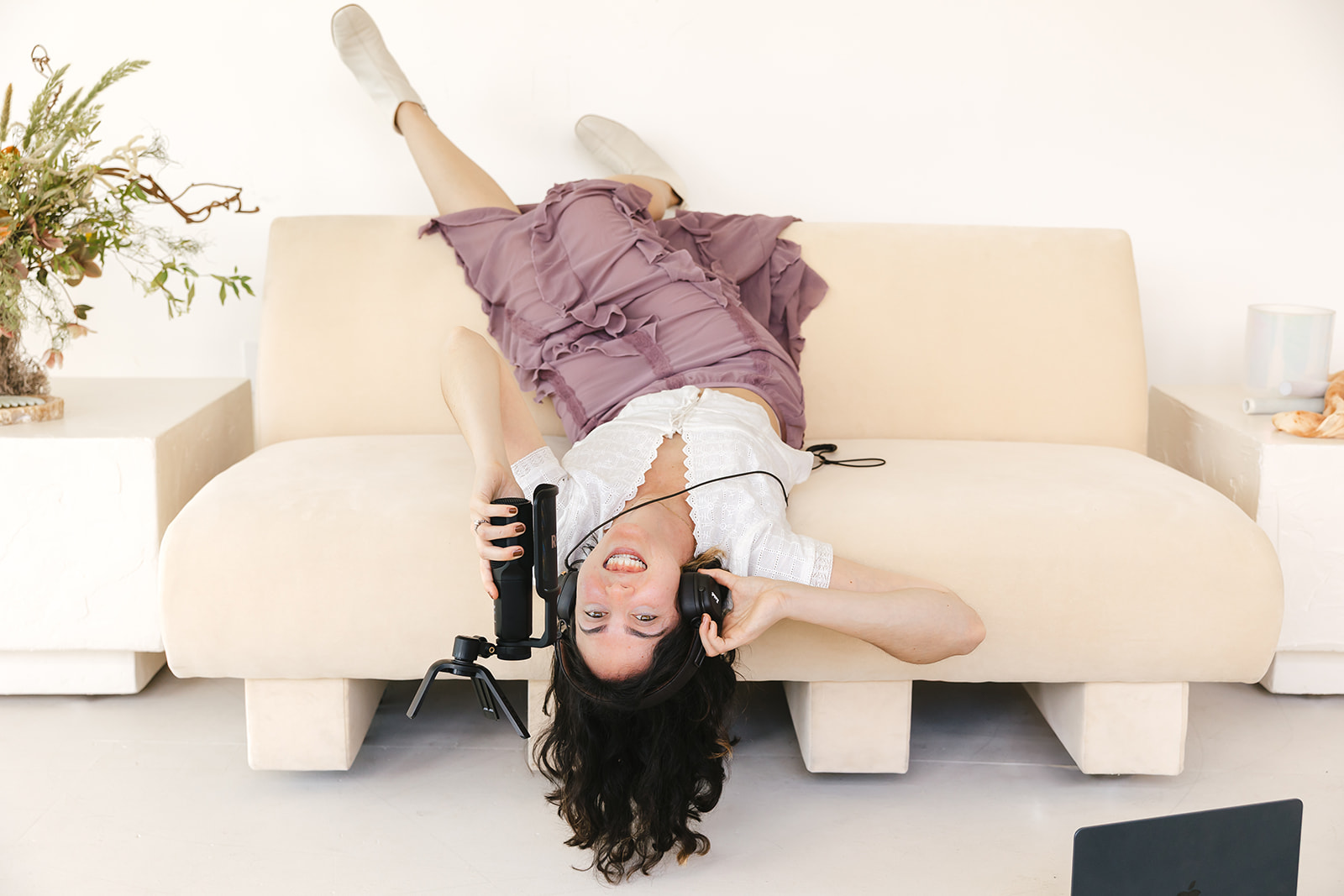 Therapist laying upside down on a couch while holding a microphone with headphones on.