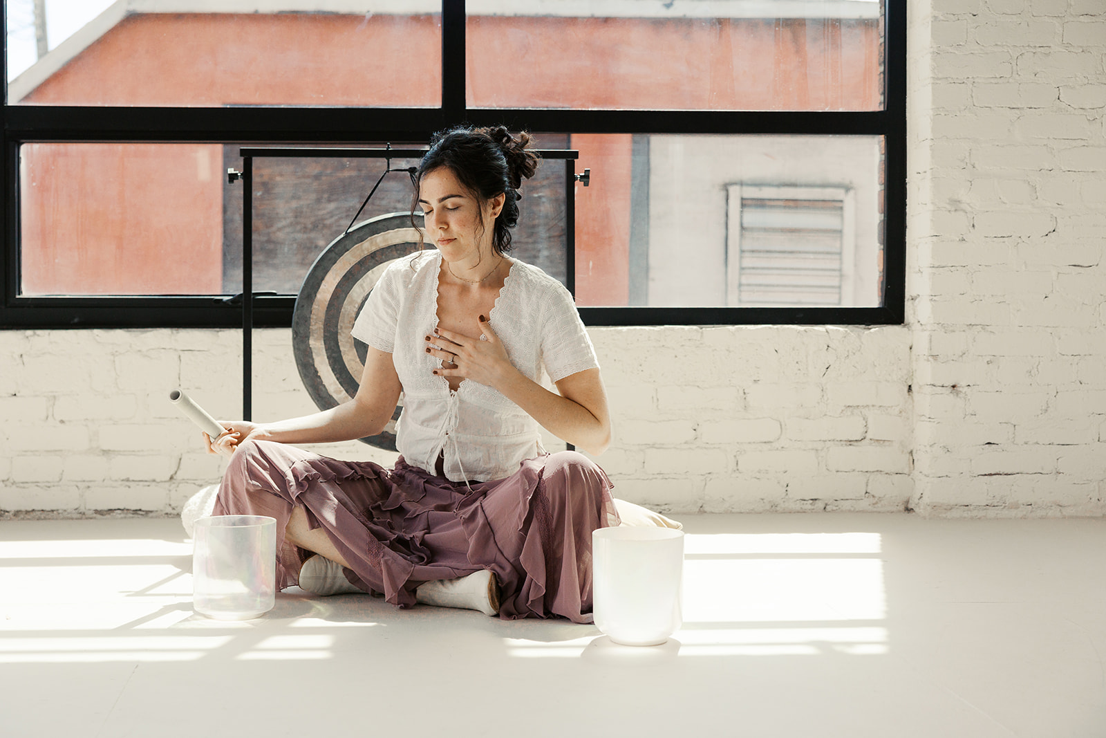 Bay Area therapist sitting with sound bowls and a gong in a light-filled studio.