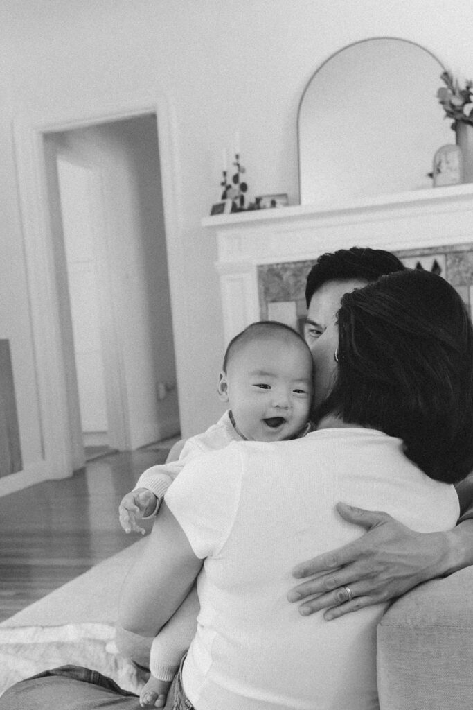Black and white photo of a couple holding their baby while they sit on the couch.