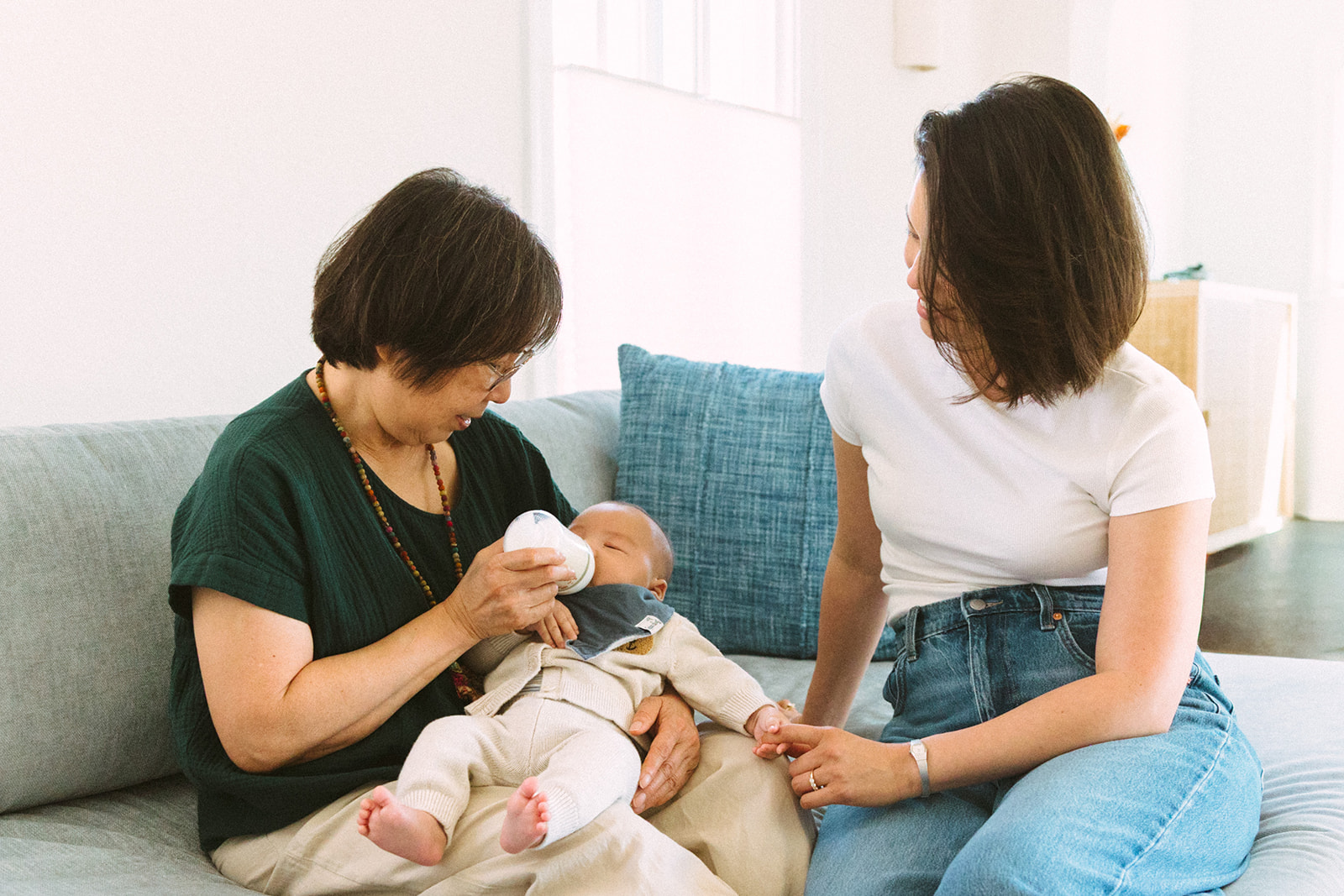 Grandmother feeding her grandson while the baby's mother sits nearby holding the babys hand. 